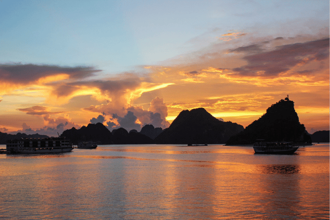 Ha Long Bay at sunset with a cruise ship sailing among limestone karsts.