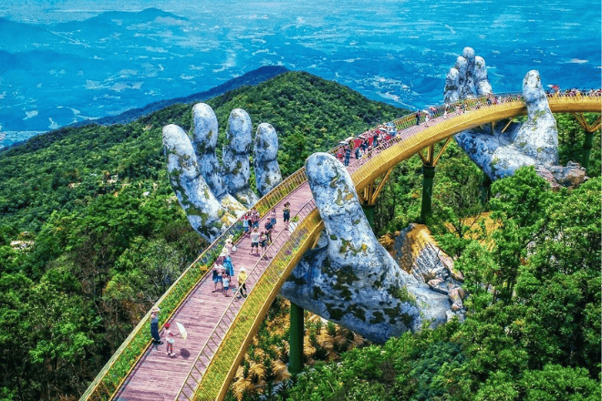 The Golden Bridge in Da Nang, supported by giant hands, with a scenic mountain backdrop.